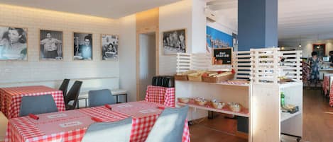 Interior de un restaurante con manteles a cuadros, sillas, un carrito de buffet y cuadros colgados en la pared.