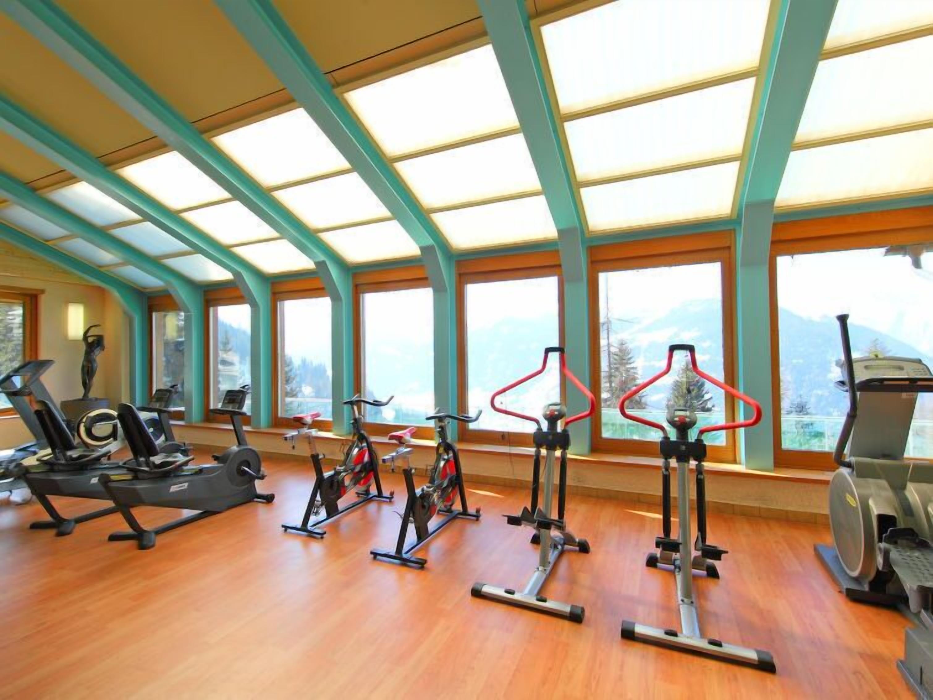 Une salle de sport équipée de divers appareils d’exercice, dotée de grandes fenêtres et d’un plancher en bois.