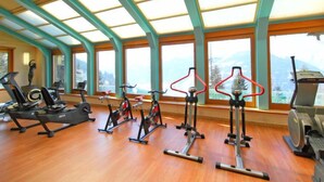 Ett gym med olika typer av träningsutrustning, stora fönster och ett trägolv.