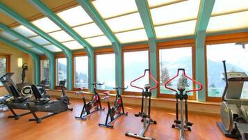 Une salle de sport équipée de divers appareils d’exercice, dotée de grandes fenêtres et d’un plancher en bois.