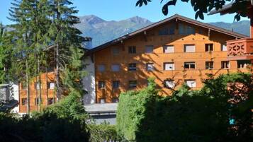 Un immeuble à plusieurs étages doté d’une façade en bois, entouré de verdure et avec des montagnes en arrière-plan.