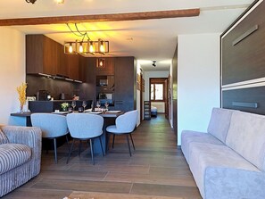 A modern kitchen with dark wood cabinets, a dining area with a table and chairs, and a living room with a sofa.