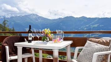 Une table dressée avec des verres à vin, une bouteille et un arrangement floral sur un balcon offrant une vue sur la montagne.