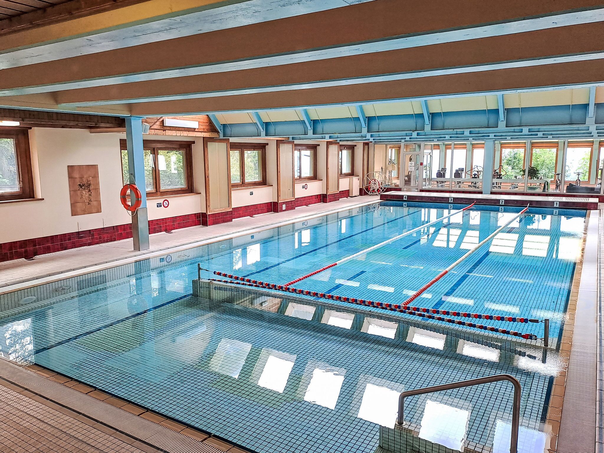 Une grande piscine intérieure avec des couloirs bien délimités, un poste de surveillance pour les sauveteurs et une vue sur l’extérieur grâce à de grandes fenêtres.