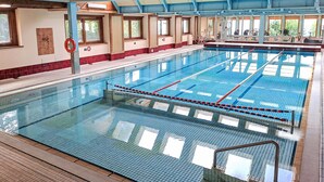 En stor inomhuspool med tydligt markerade banor, en livräddarstation och utsikt över omgivningen genom stora fönster.