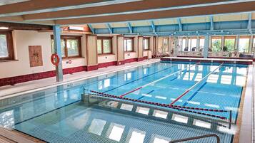 Une grande piscine intérieure avec des couloirs bien délimités, un poste de surveillance pour les sauveteurs et une vue sur l’extérieur grâce à de grandes fenêtres.