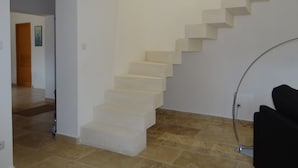 Una escalera con peldaños color beige que lleva a una plataforma, una puerta abajo y una silla negra a la derecha.