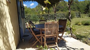 Un patio al aire libre con mesa y sillas de madera, rodeado de follaje y vistas a un paisaje exuberante.