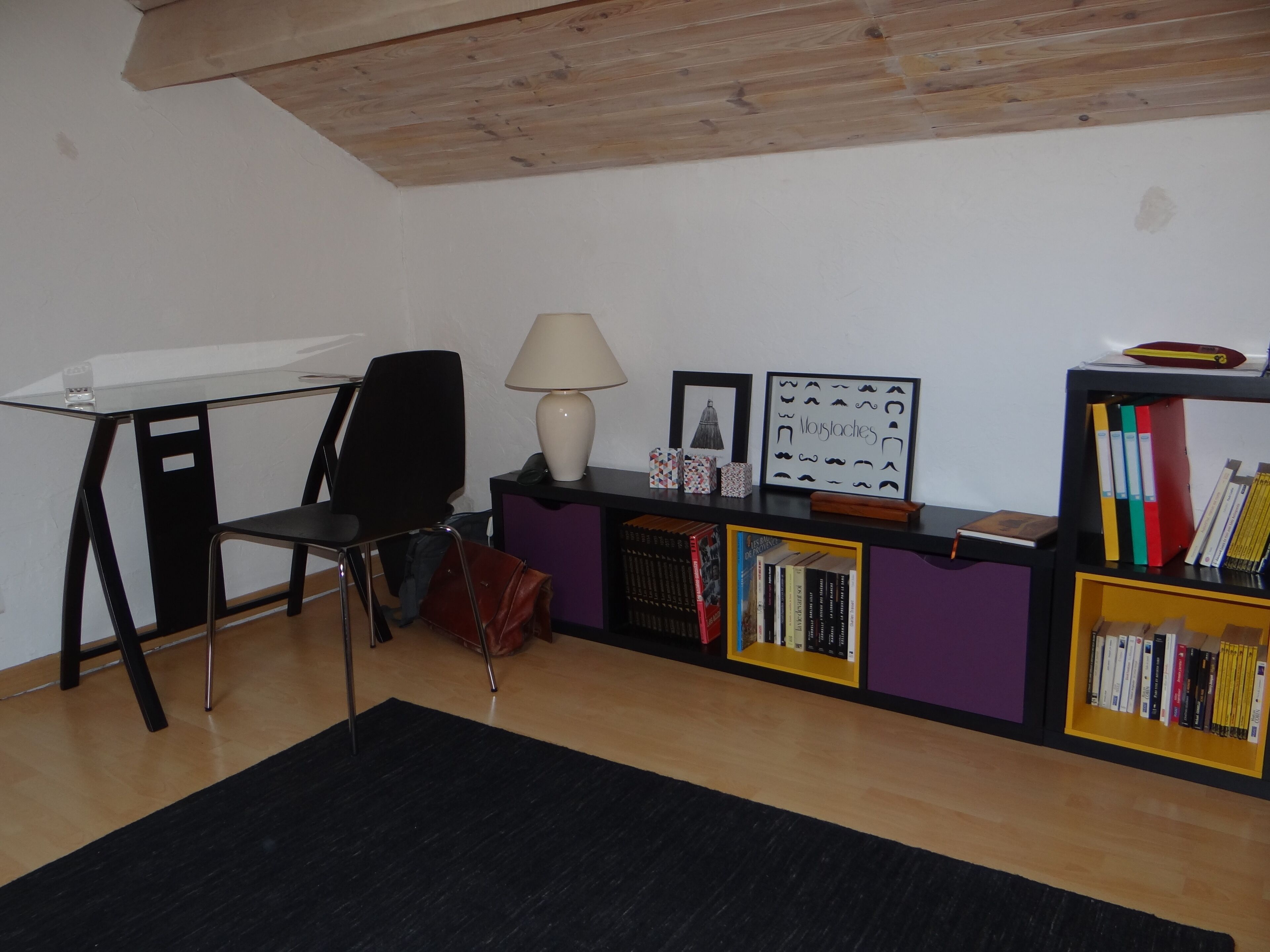 A study room with a desk, chair, lamp, bookshelf, and framed pictures.