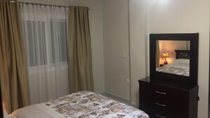 Ein Schlafzimmer mit einem Bett, einem Schminktisch, einem Spiegel und einem Fenster mit Vorhängen.