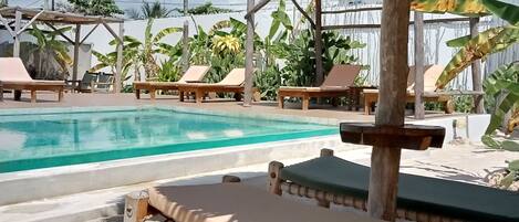 A pool area with lounge chairs and a thatched roof structure.