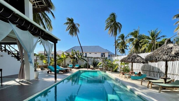 A swimming pool with lounge chairs and palm trees. - Villa Huruma (Paje)