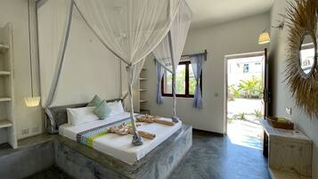 Un dormitorio con cama a dosel, un pequeño banco de madera, un espejo y vistas al exterior.