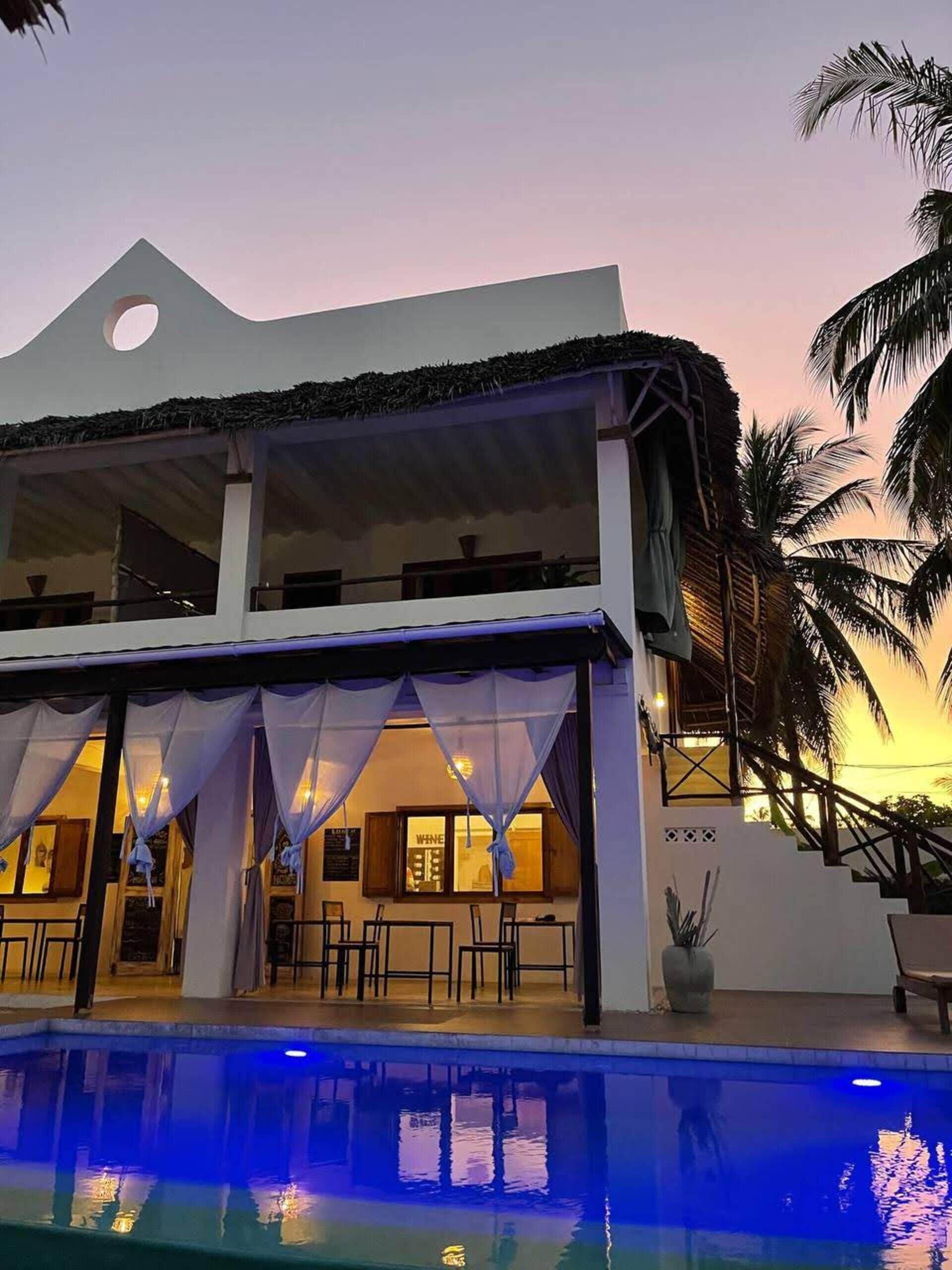 A two-story building with a pool, outdoor seating, and palm trees.