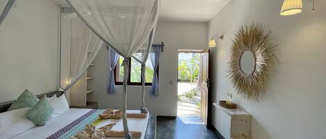 A bedroom with a bed, a canopy, a bedside table, a mirror, and a view of the outside.