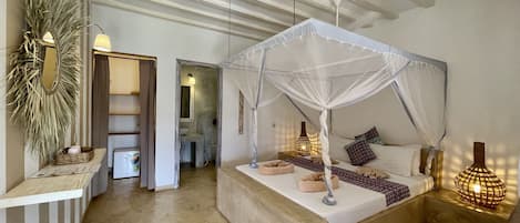 A bedroom with a canopy bed, bedside lamps, a small bedside table, and a large mirror.
