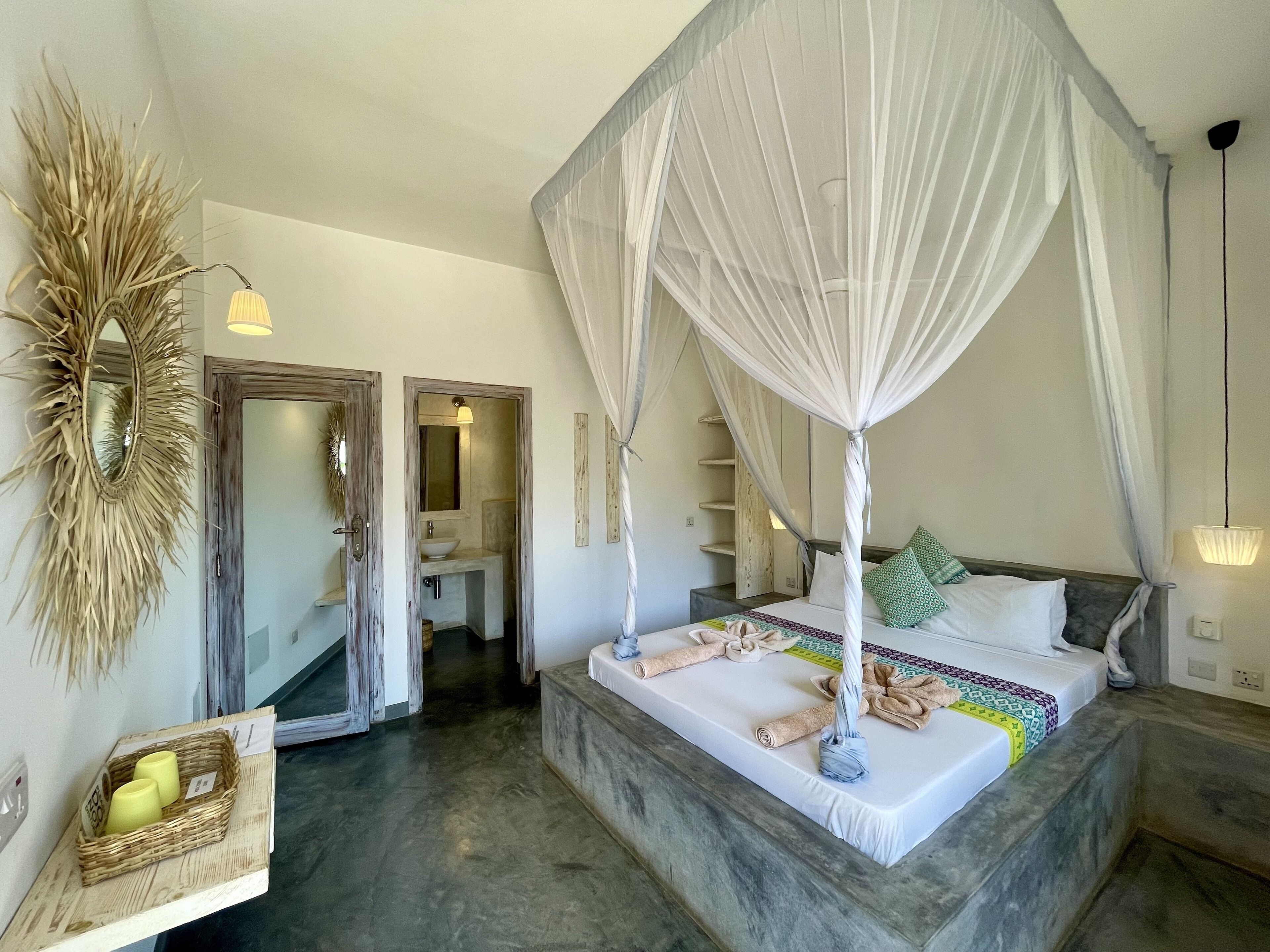 A bedroom with a four-poster bed, a small bathroom, and a mirror with a decorative frame.
