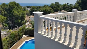 A balcony with a white balustrade overlooking a swimming pool and a view of the sea and surrounding greenery. - Beautiful villa, swimming pool, tennis court, basketball court, garden, sea view, near beaches (El Vendrell)