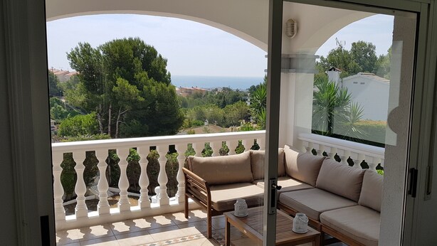 A balcony with a sofa and a table, overlooking a scenic view of trees and buildings. - Beautiful villa, swimming pool, tennis court, basketball court, garden, sea view, near beaches (El Vendrell)