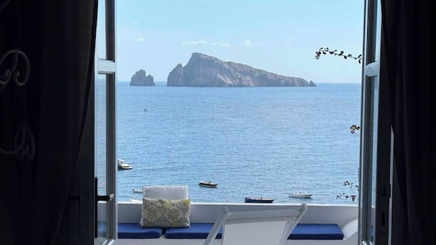 An open balcony with a view of the sea, a white chair, and a cushion.