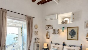 A bedroom with a bed, a nightstand, a lamp, a wall-mounted air conditioner, and a window with curtains.