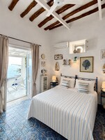 Un dormitorio con cama, mesita de noche, lámpara, aire acondicionado instalado en la pared y ventana con cortinas.