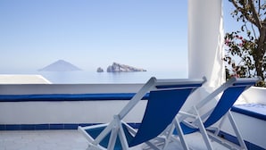 A balcony with two blue and white lounge chairs, a white column, and a view of a distant island.