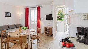 A modern kitchen with a coffee maker, a dining table with chairs, a TV mounted on the wall, and a view of the garden through the window.