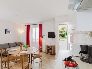 A modern kitchen with a coffee maker, a dining table with chairs, a TV mounted on the wall, and a view of the garden through the window.