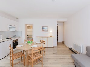Une cuisine moderne avec des meubles blancs, une table à manger avec des chaises, et une vue sur le salon.