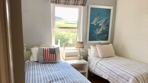 A bedroom with two beds, a window with a view of greenery, a painting of sailboats, and a lamp on a bedside table. - Holiday home sleeps 6 central,  10 minute walk to golf course (Lahinch)