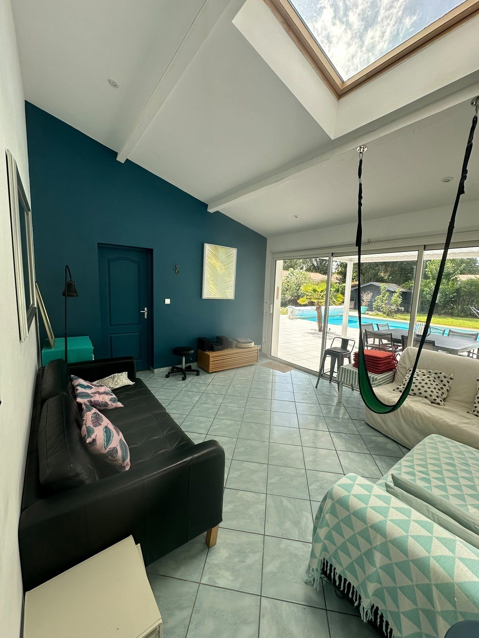 Un salon moderne avec un canapé noir, un fauteuil suspendu et une vue sur une piscine.