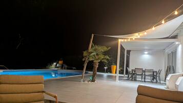 An outdoor patio area with a pool, lounge chairs, and string lights.