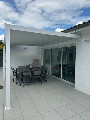 A covered patio area with a table and chairs, a sliding glass door, and a white exterior wall.