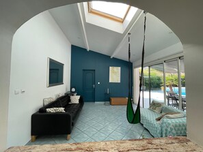 A modern living room with a black sofa, a blue accent wall, a hanging chair, and a view of a swimming pool through large sliding glass doors.