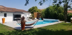 A backyard with a swimming pool, a hammock, and a patio area with outdoor furniture.