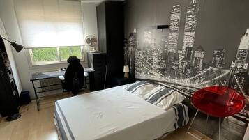 A modern bedroom with a large bed, a desk, and a cityscape mural on the wall.