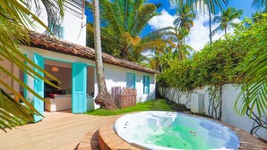 A backyard with a hot tub, a wooden deck, and a house with blue shutters. - Pousada Patacho (Porto de Pedras)