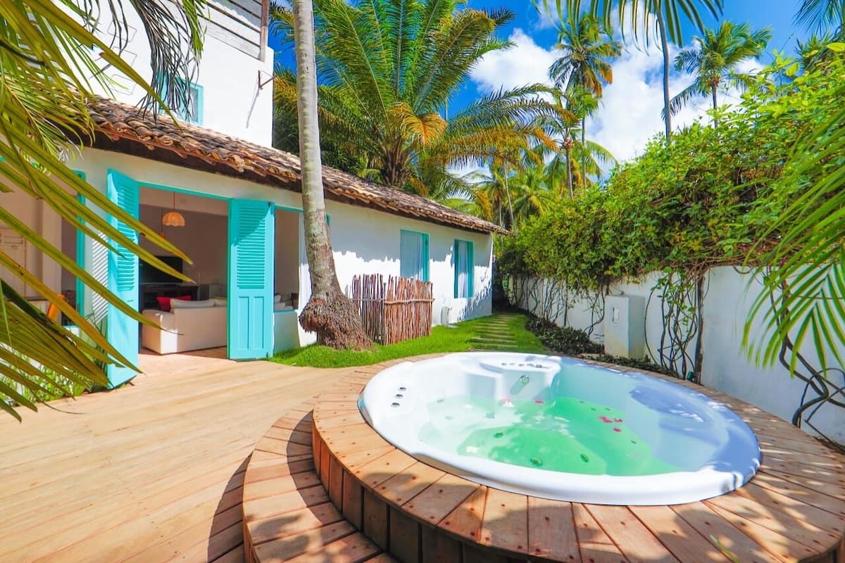 Un patio trasero con un jacuzzi, una terraza de madera y una casa con contraventanas azules.