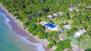 An aerial view of a beach resort with a swimming pool, palm trees, and beachfront properties. - Pousada Patacho (Porto de Pedras)