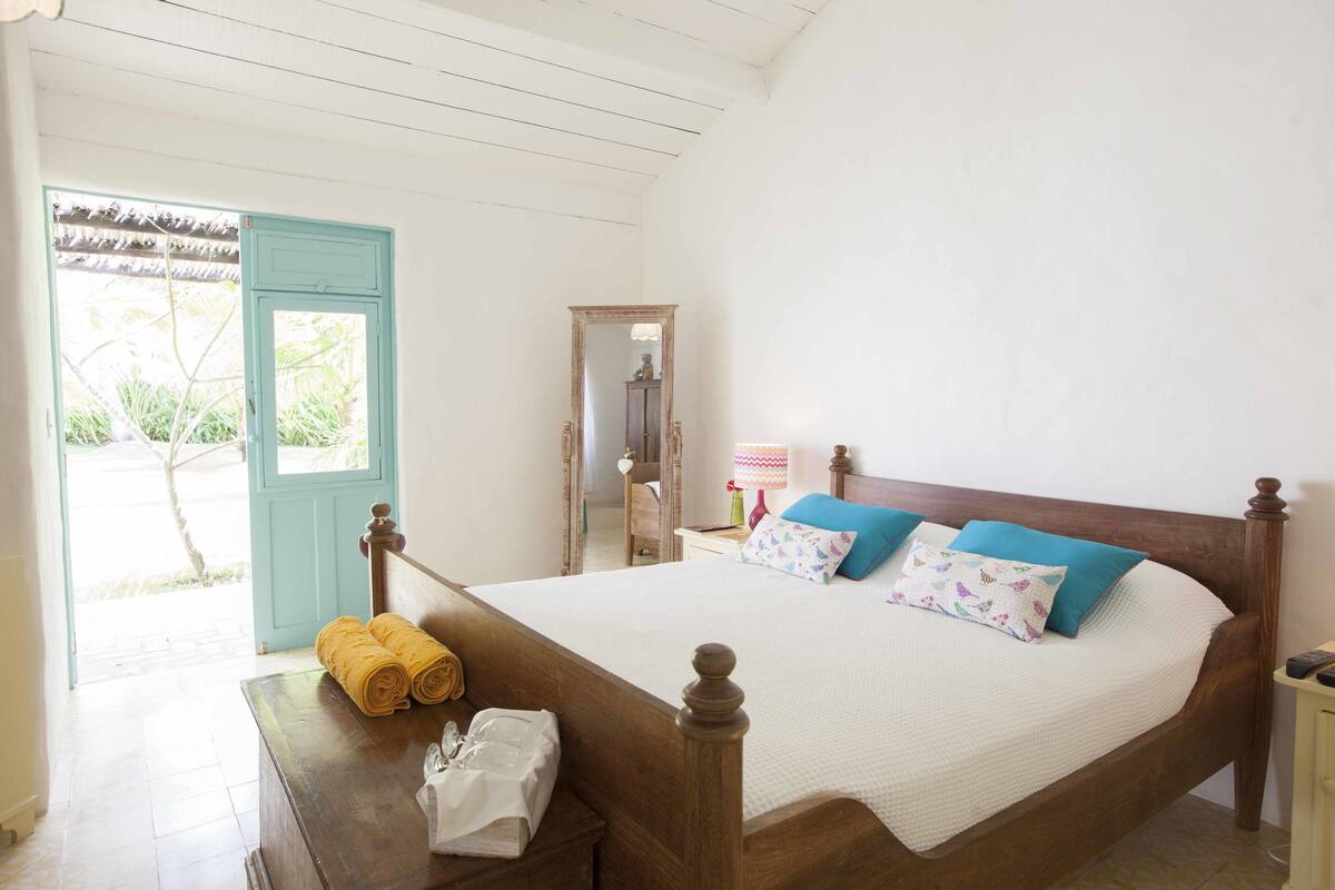 Un dormitorio con cama de madera, una mesita de noche, un espejo y una ventana con vistas a zonas verdes.