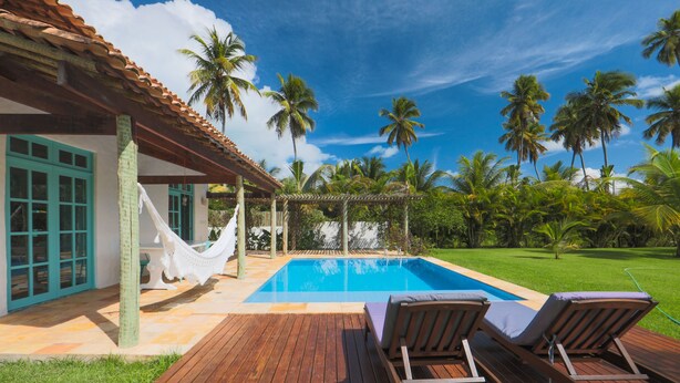 A wooden deck with a pool, lounge chairs, and a hammock. - Pousada Patacho (Porto de Pedras)
