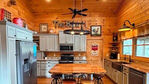 A cozy cabin-style kitchen with wooden walls, a central island with stools, a refrigerator, stove, microwave, and a ceiling fan. - Deep Creek Waterfront Home • Hot Tub • Pool Table • Minutes to Downtown & GSMNP (Bryson City)
