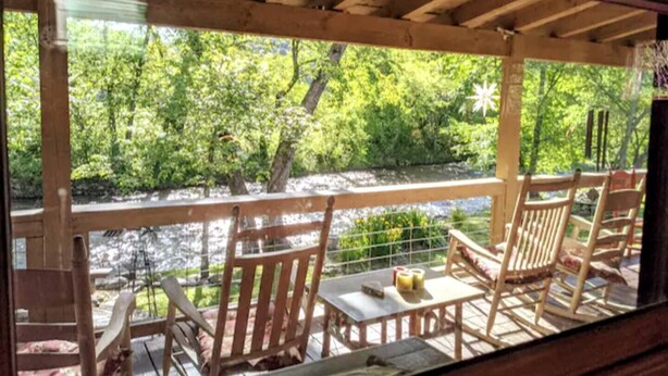 A wooden deck with chairs and a table, overlooking a river and greenery. - Deep Creek Waterfront Home • Hot Tub • Pool Table • Minutes to Downtown & GSMNP (Bryson City)