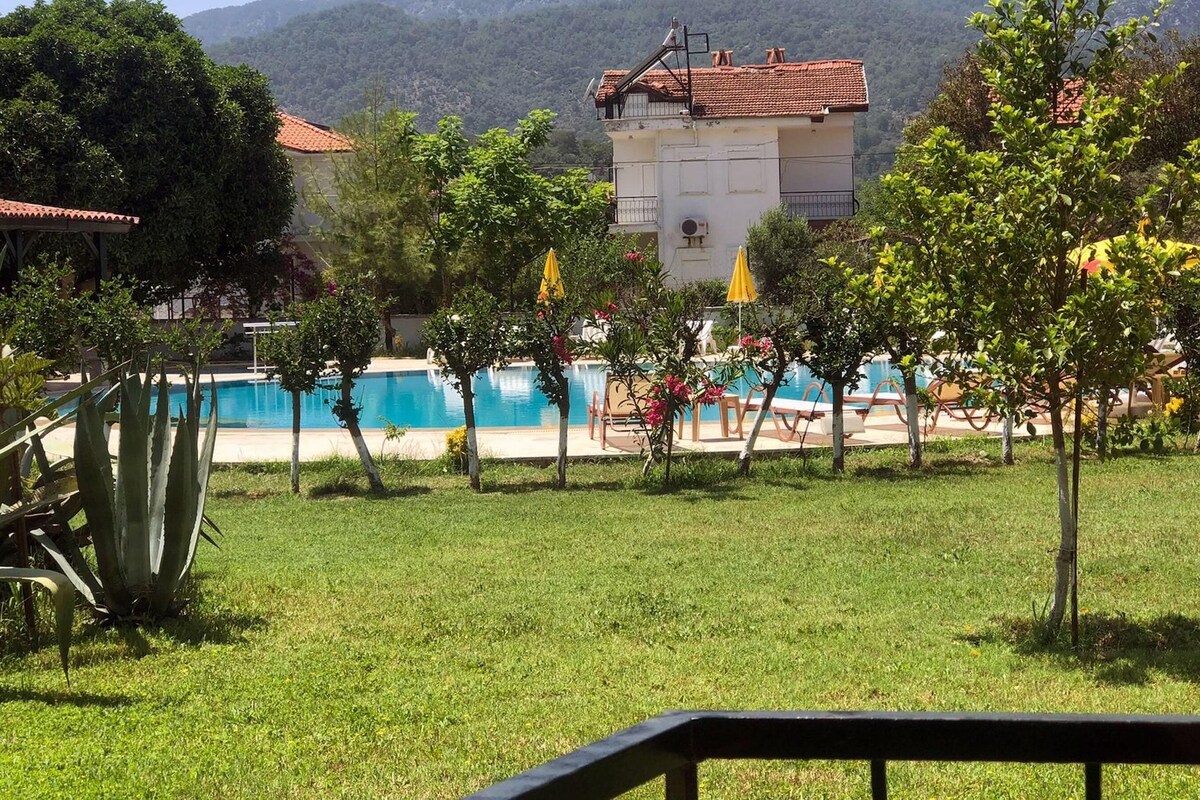 A pool area with a view of a building and mountains in the background.