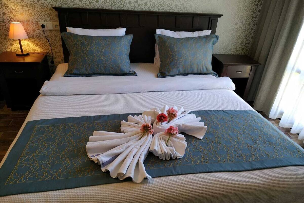 A neatly made bed with a blue and white patterned bedspread, two matching pillows, and a decorative towel arrangement with flowers on a blue bedspread.