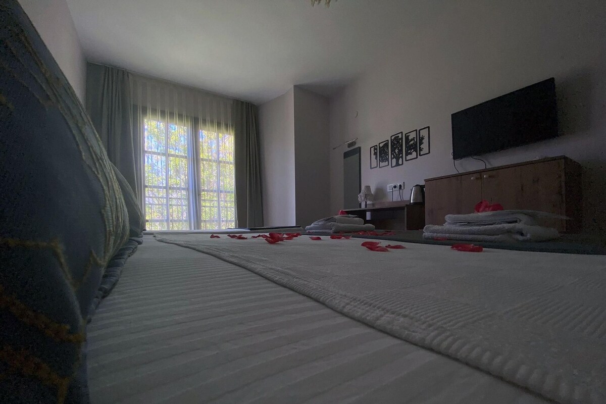Una camera d'albergo con un letto grande, una televisione a schermo piatto montata sulla parete e una finestra con tende.