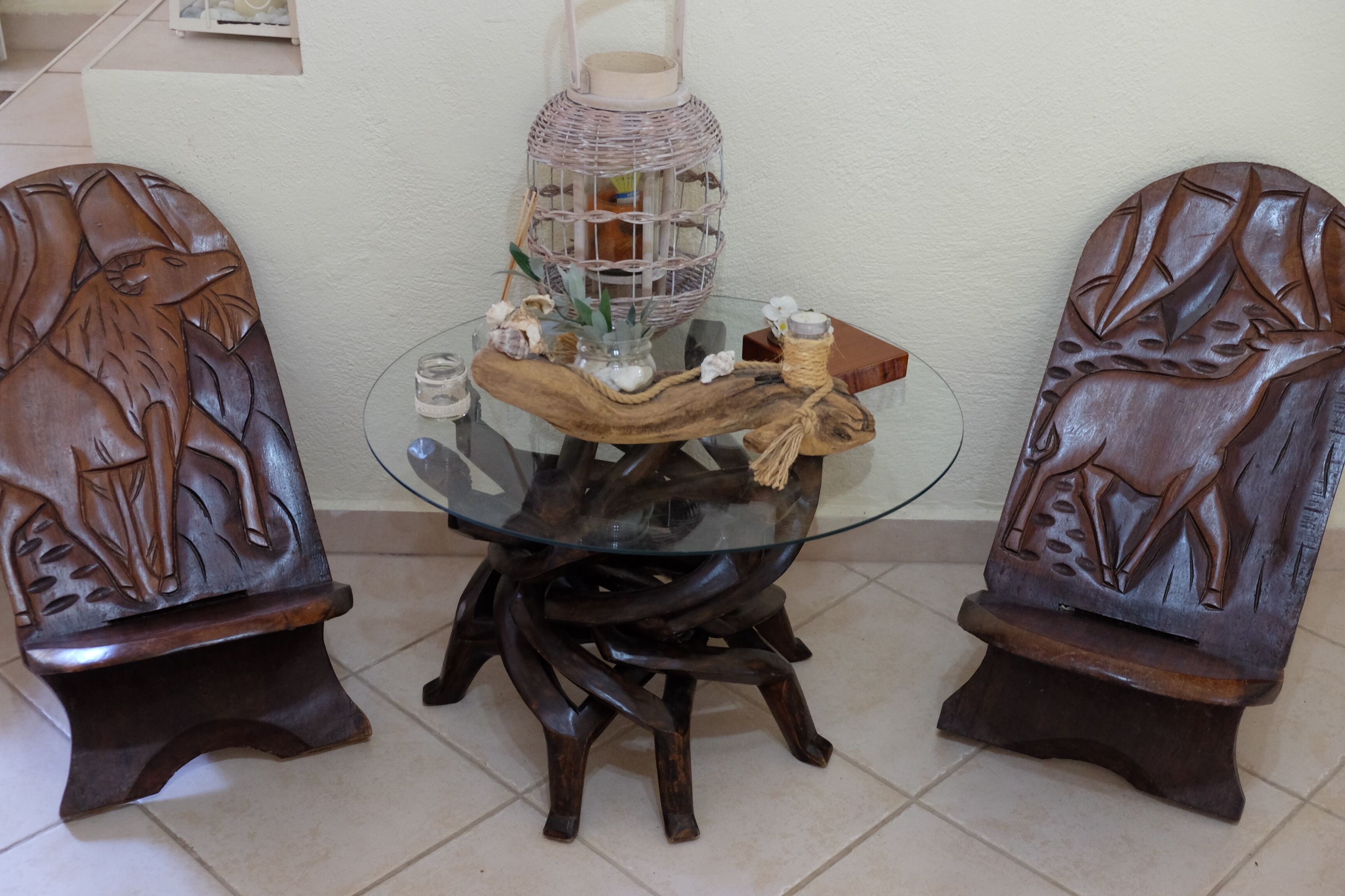A round glass table with a wooden base, surrounded by two intricately carved wooden chairs.