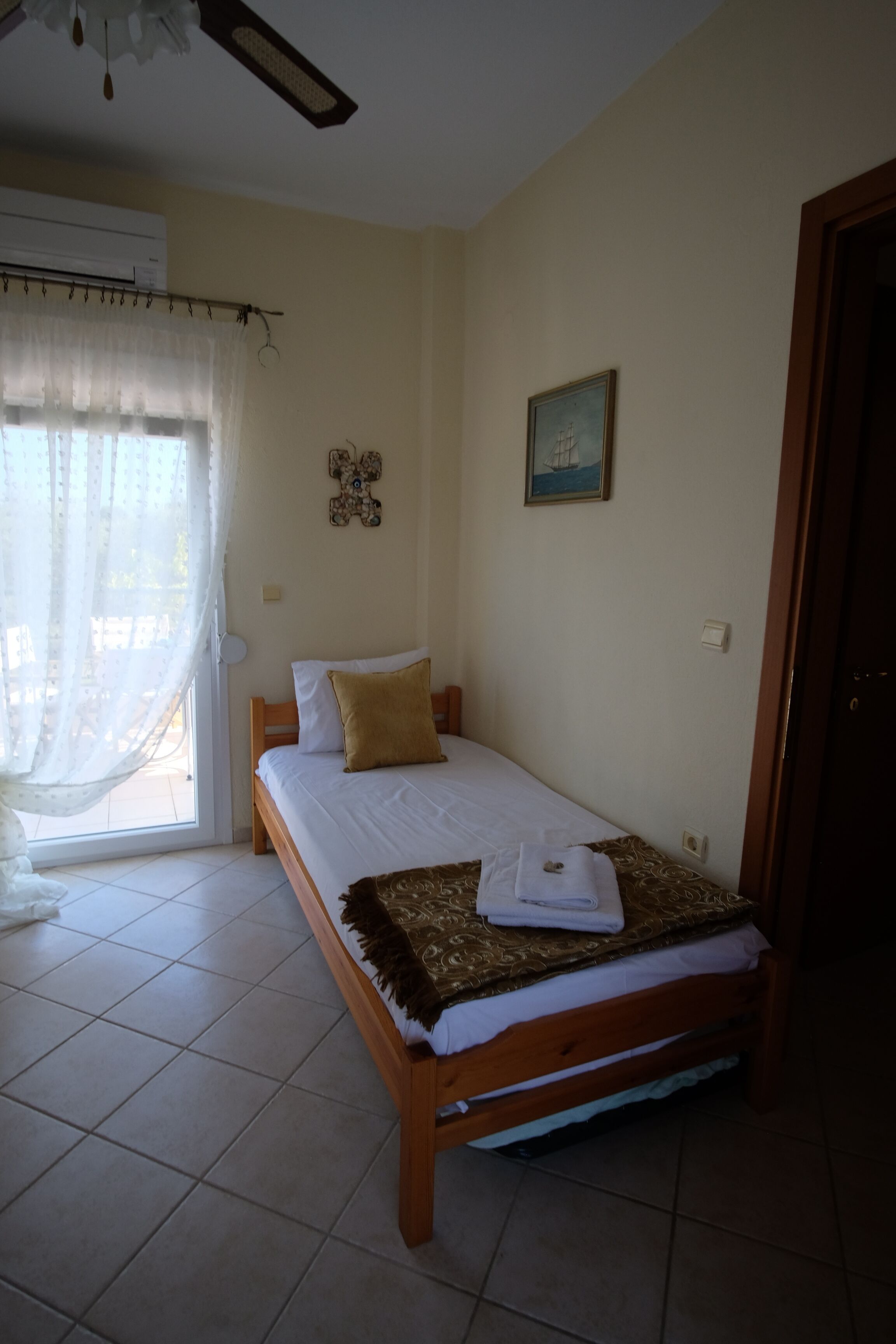 A bedroom with a bed, a window with curtains, a ceiling fan, and a door.