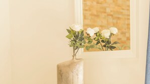 Ett sovrum med en säng, ett nattduksbord med en vas med vita blommor, en byrå och en inramad tavla på väggen.